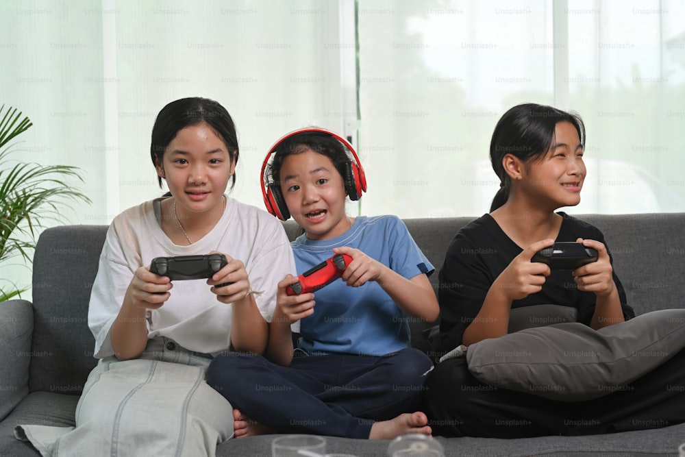 Happy Asian girls sitting together on sofa at home and playing video games.