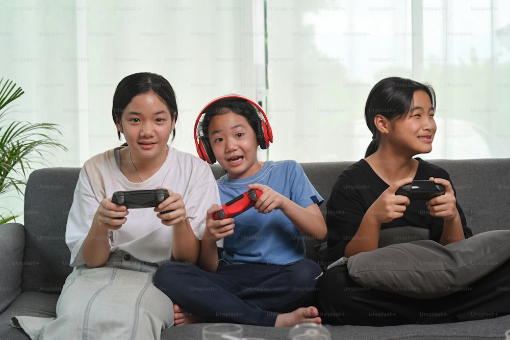 Chicas asiáticas felices sentadas juntas en el sofá de casa y jugando videojuegos.