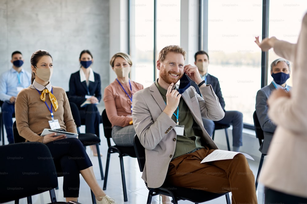 Glücklicher männlicher Unternehmer, der die Schutzmaske abnimmt, während er an einer Geschäftskonferenz im Sitzungssaal teilnimmt.