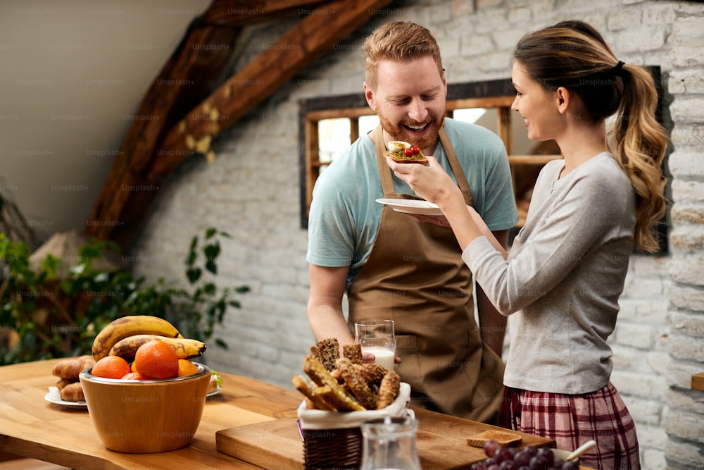 Happy woman feeding her boyfriend while having breakfast in the morning together.