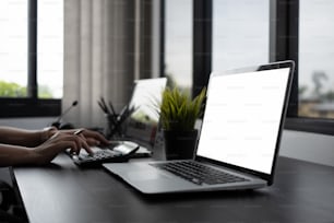 Vista ravvicinata del computer portatile e mano del contabile che utilizza la calcolatrice sul tavolo di legno nero in ufficio.