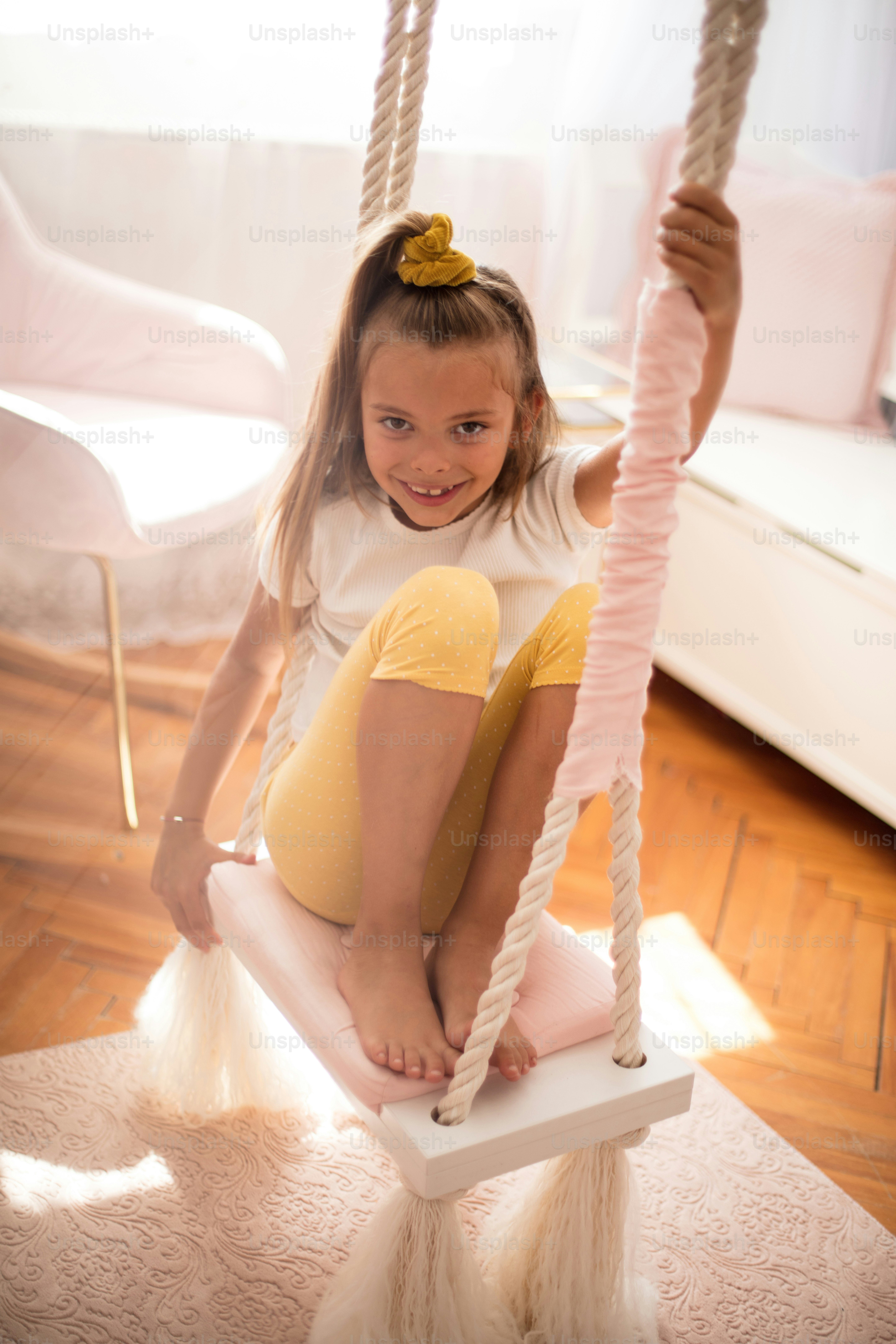 Portrait de petite fille souriante sur balançoire dans sa chambre.