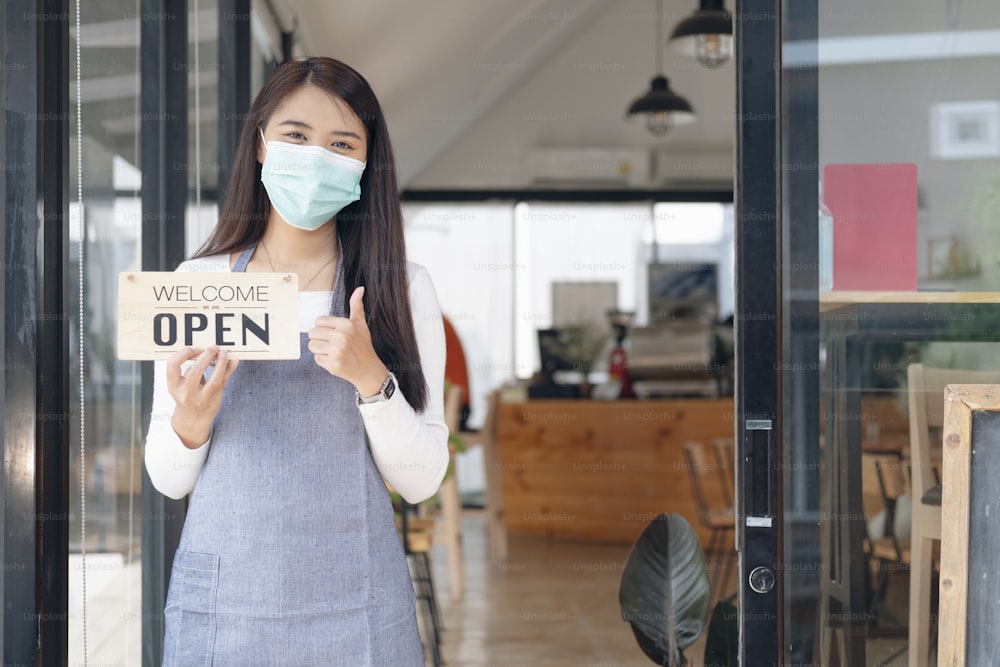 Reopen, Young Asia girl wear face mask turning a sign from closed to open sign after lockdown.