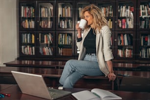 Young attractive businesswoman using a laptop while drinking coffee in her office