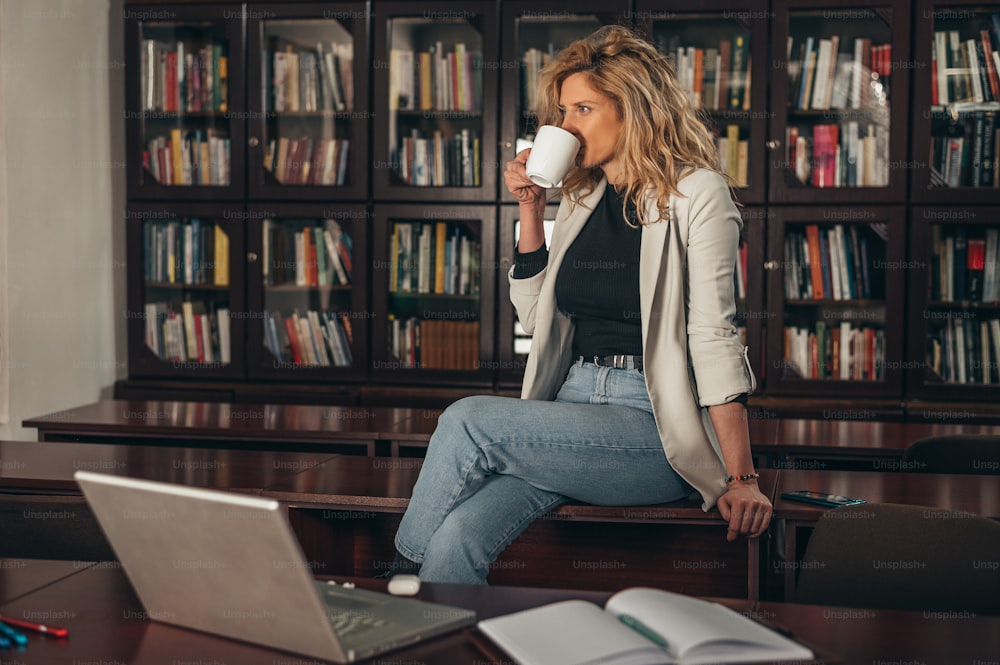 Young attractive businesswoman using a laptop while drinking coffee in her office