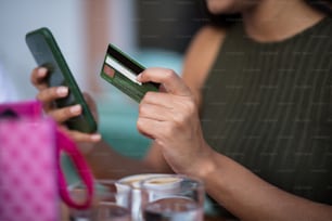Donna che utilizza lo smartphone e la carta di credito per lo shopping online in caffetteria. L'attenzione è rivolta alla carta di credito.