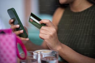 Woman using smart phone and credit card for shopping online in coffee shop. focus is on credit card.