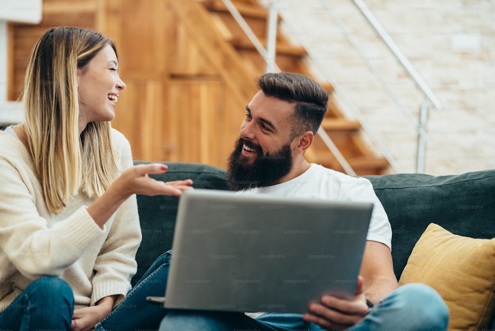 Young beautiful couple using a laptop while relaxing together on the sofa at home