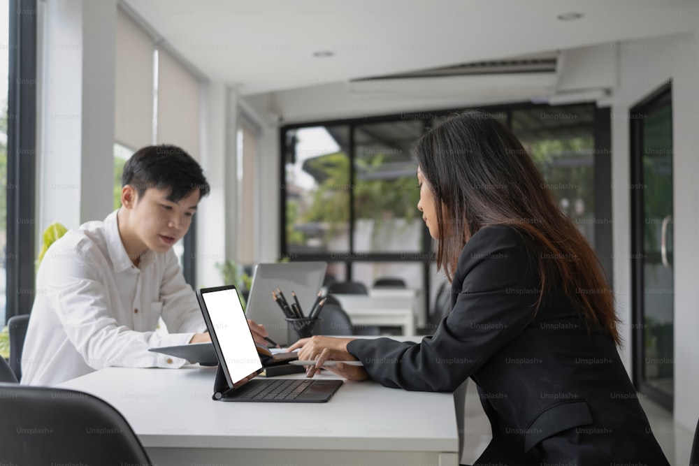 Dos jóvenes empresarios asiáticos trabajando juntos en una oficina moderna.