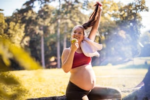 Pregnant woman eating apple after exercise in the park.
