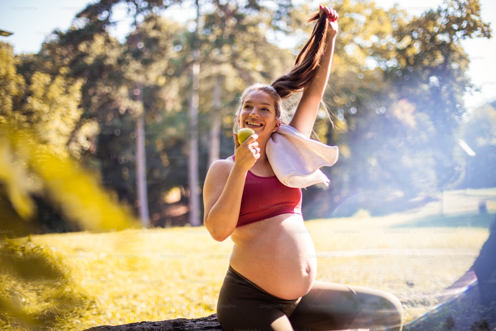 Pregnant woman eating apple after exercise in the park.