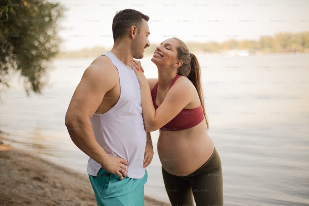 Young smiling man and pregnant woman on the beach.