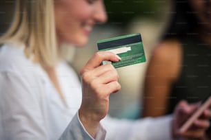 Two women in café. Woman using credit card and mobile phone. Focus is on credit card.