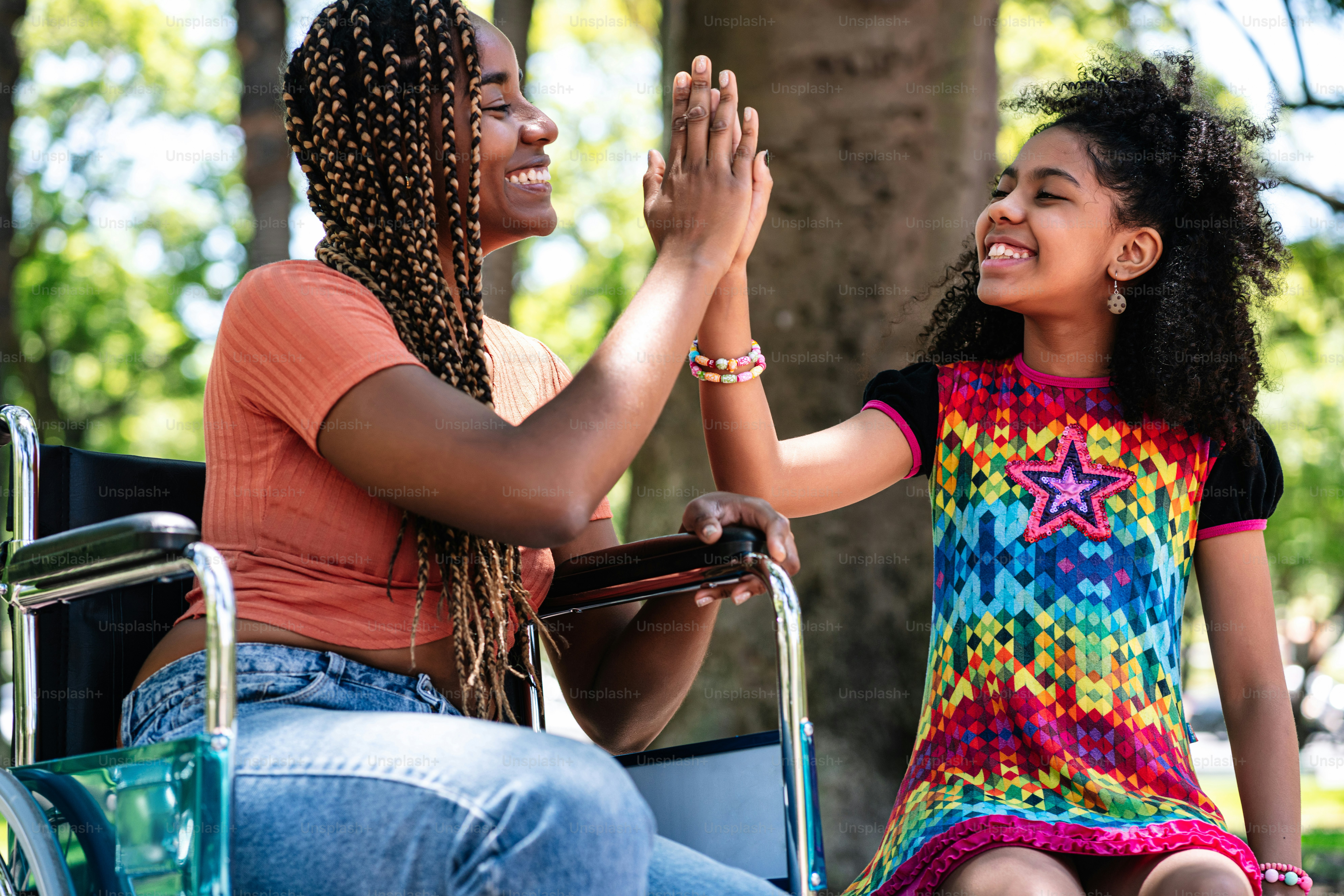 An african american woman in a wheelchair enjoying a day at the park and having fun with her daughter.