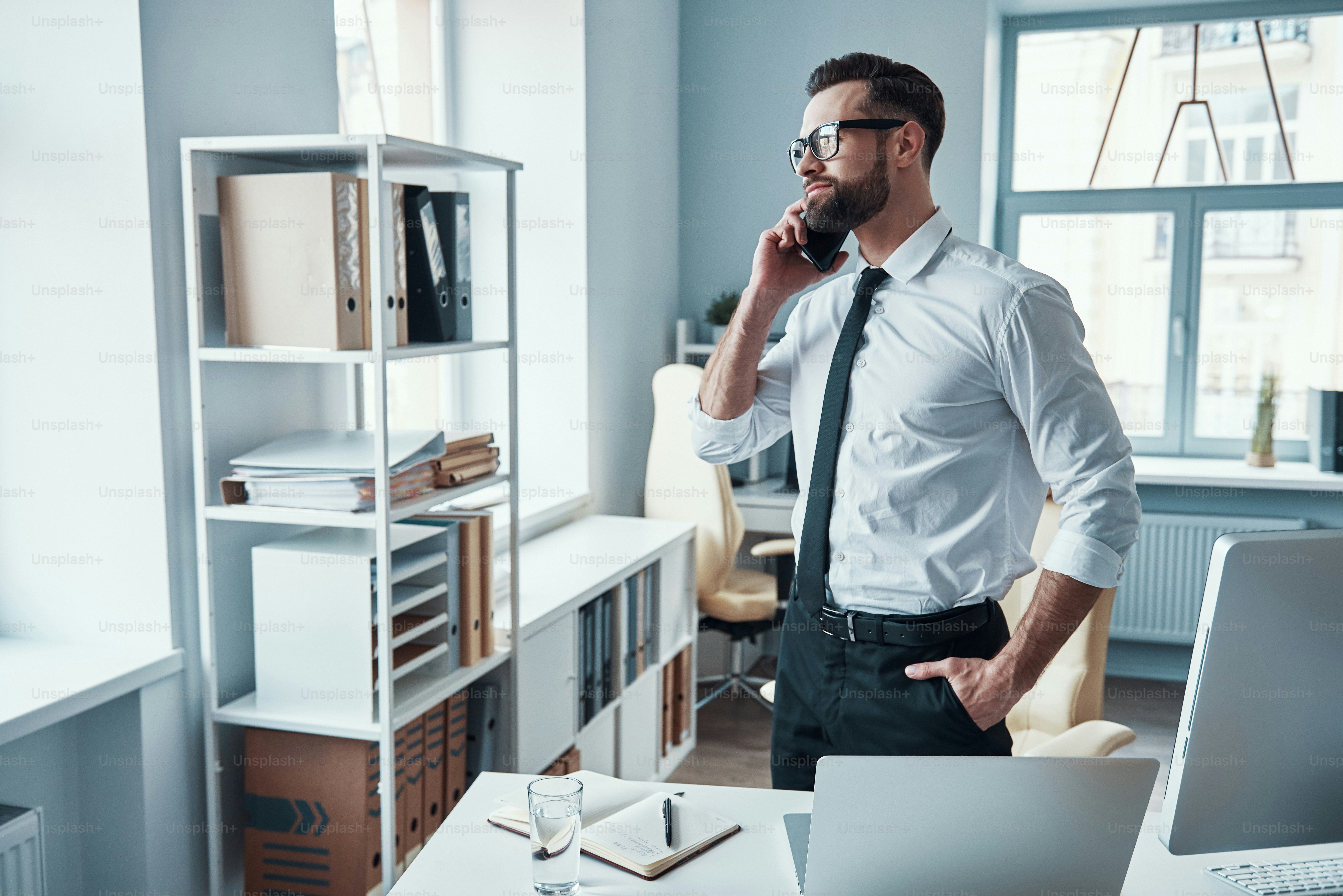 Handsome young man in formalwear talking on the phone and smiling while working in the office