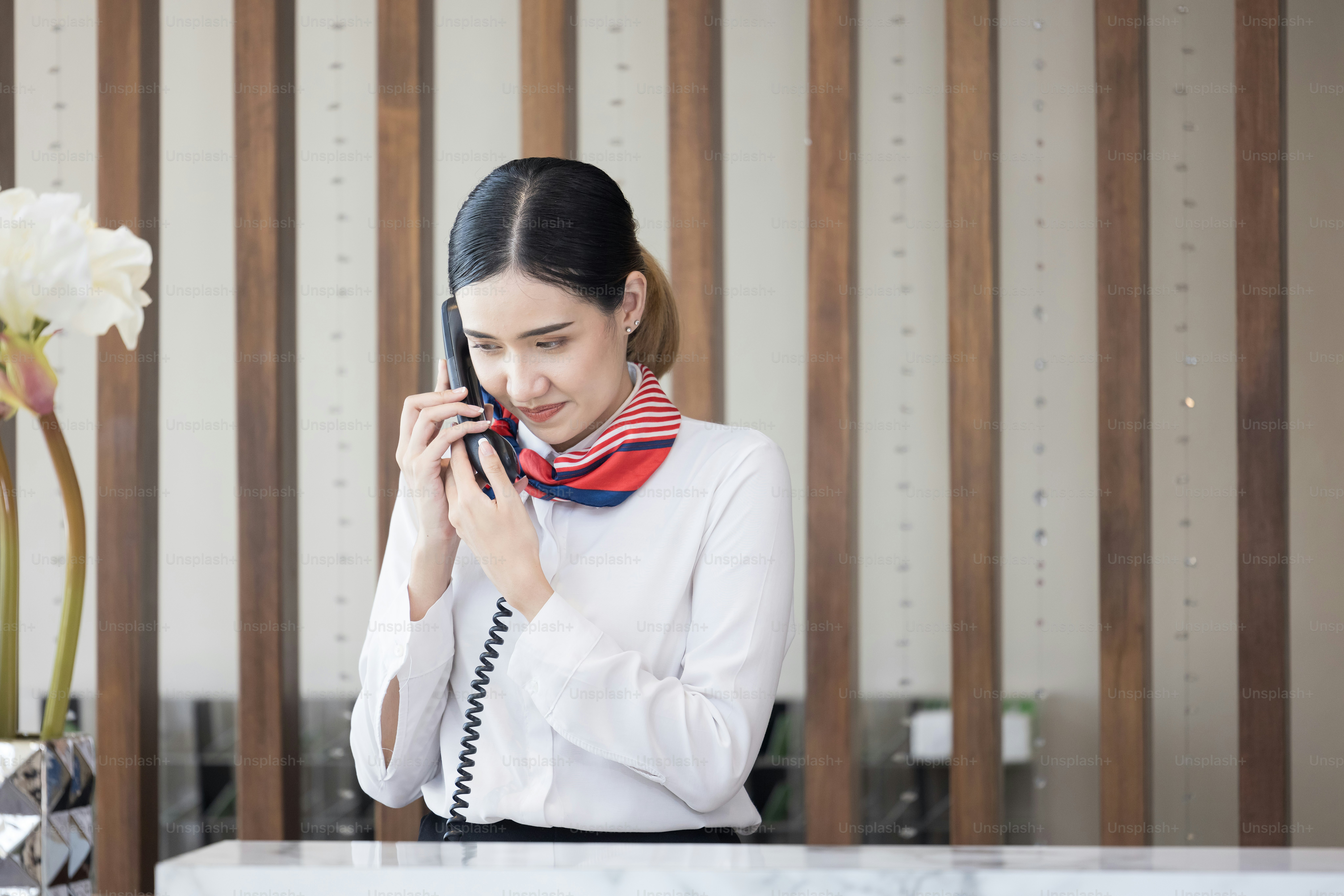 Bienvenido al hotel, joven joven mujer asiática feliz recepcionista de hotel que sonríe de pie, ella toma una llamada telefónica en un mostrador de recepción de lujo moderno que espera a los huéspedes que obtienen la tarjeta de acceso en el hotel