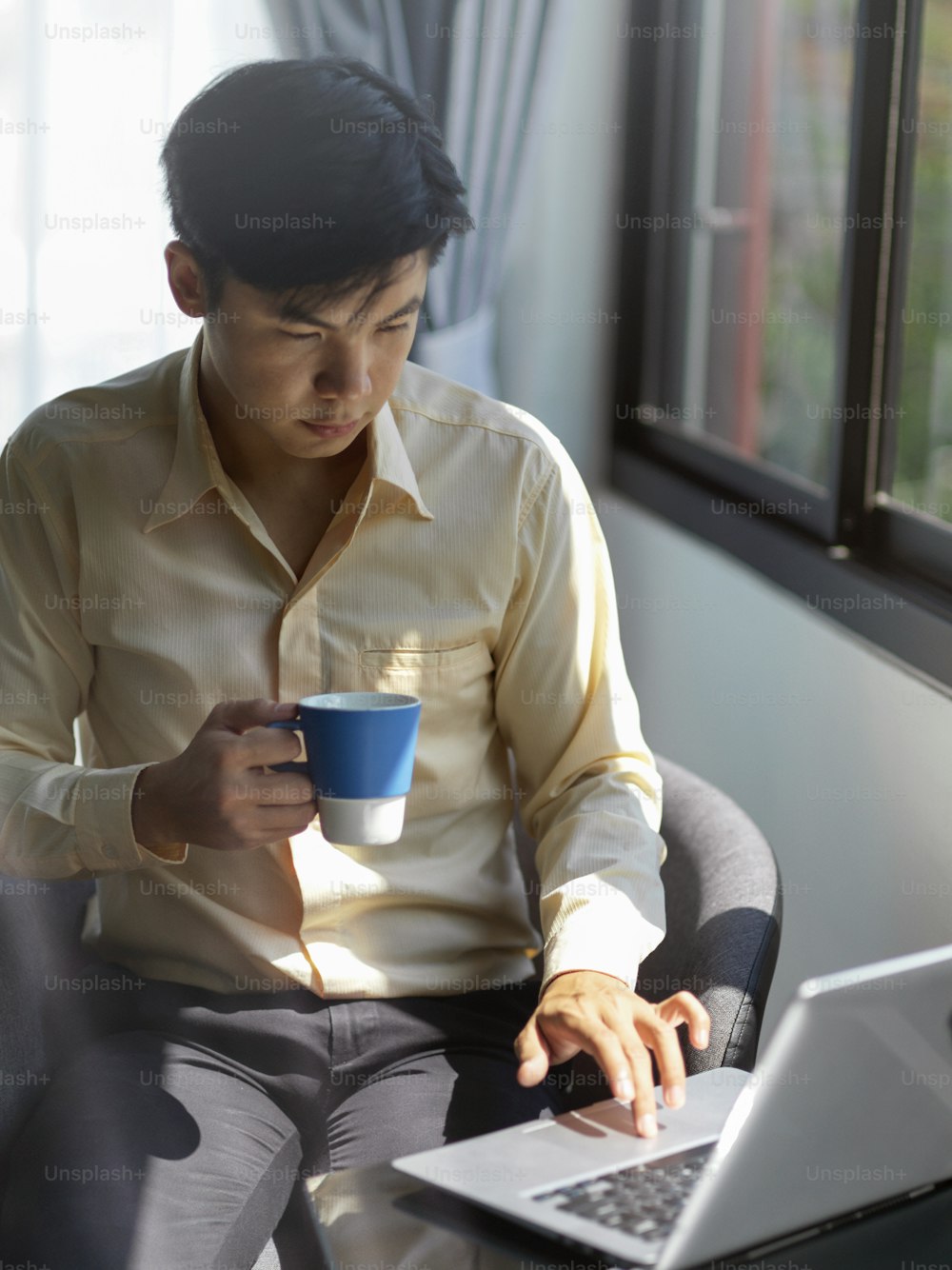 Young businessman working with laptop computer while holding a cup of coffee in his office room