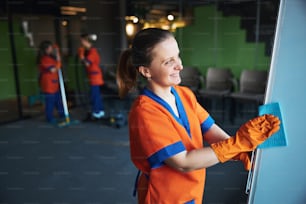 Vista lateral de una joven trabajadora sonriente limpiando la pizarra con un paño húmedo