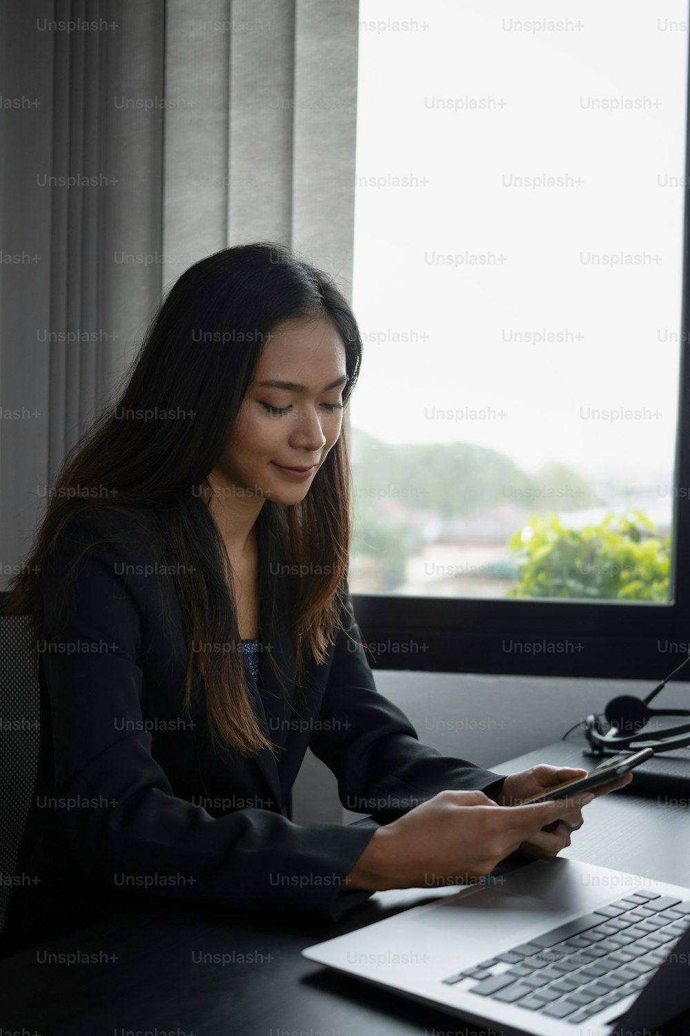 Ritratto di affascinante donna d'affari seduta vicino alla finestra in ufficio e utilizzando il telefono cellulare.