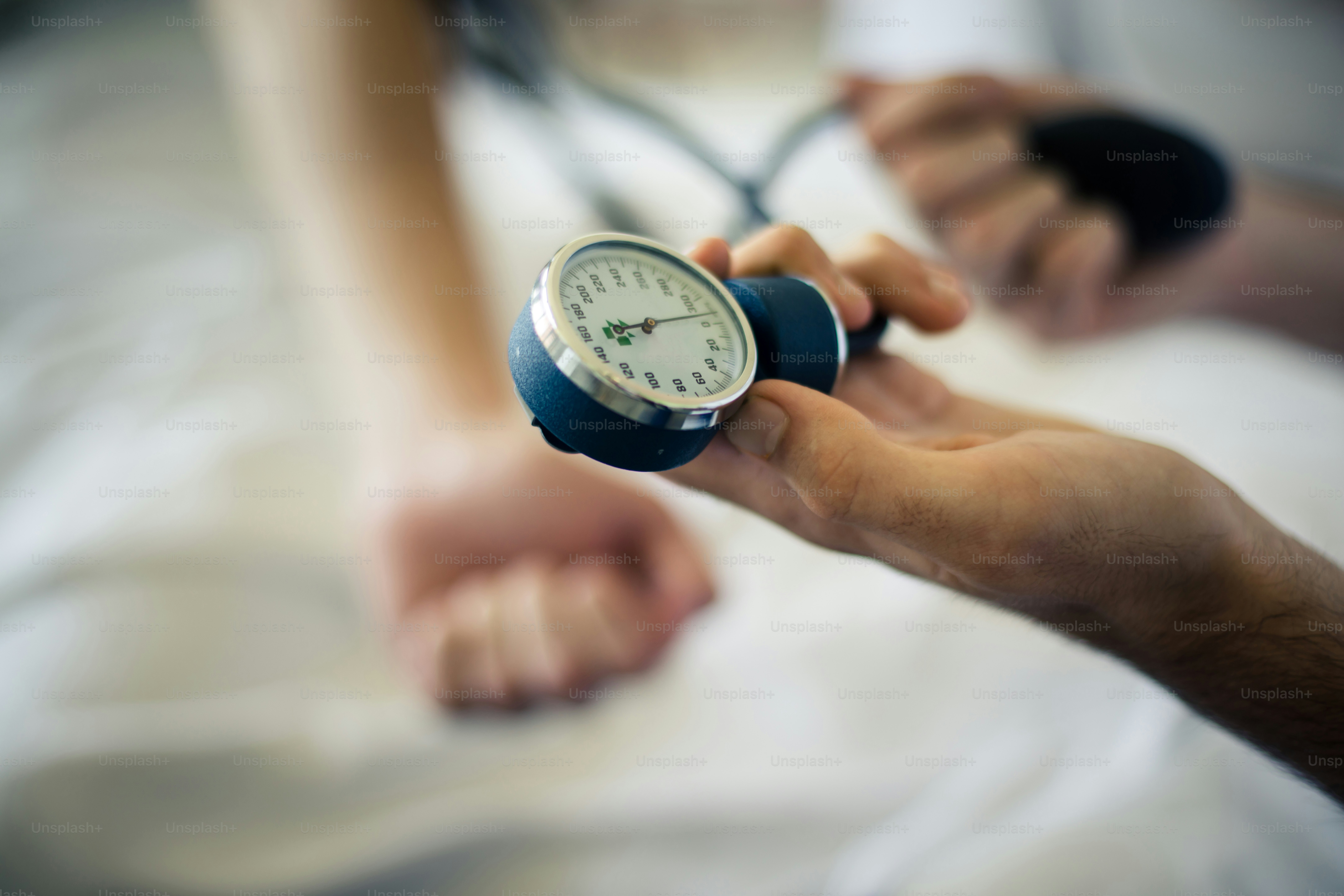 Der Arzt misst den Druck des Patienten mit einem Stethoskop. Aufschließen. Der Fokus liegt auf den Händen.