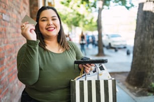 Portrait d’une jeune femme grande taille tenant une carte de crédit et des sacs à provisions à l’extérieur dans la rue. Concept de shopping et de vente.