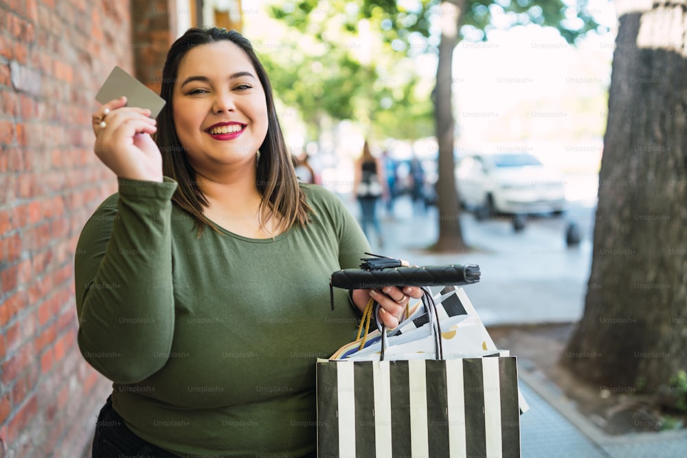 路上で屋外でクレジット カードとショッピング バッグを保持しているプラスのサイズの若い女性の肖像画。ショッピングと販売のコンセプト。