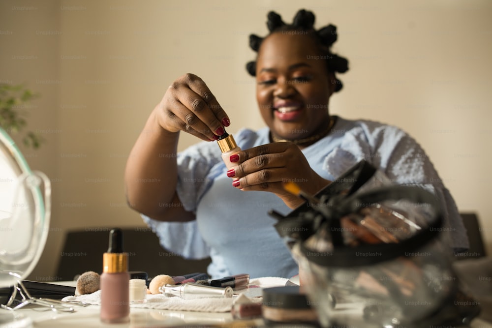 Choose the tone of the foundation. Portrait view of the multiracial woman blogger holding different concealers and showing it to the camera while making online tutorial for her subscribers at home