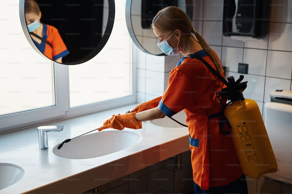 Vista lateral de una trabajadora con una mascarilla desechable haciendo la limpieza de desinfección