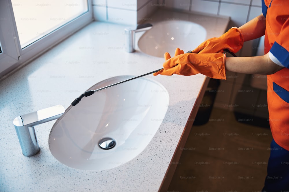 ゴム手袋をはめた女性清掃員が洗面台に消毒液を噴霧しているトリミングされた写真