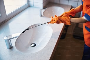 Cropped photo of a female cleaner in rubber gloves spraying the washbasin with a disinfectant