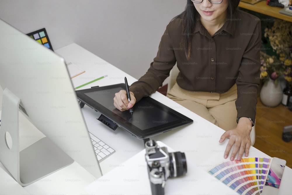 Abgeschnittene Aufnahme einer kreativen Frau, die mit einem Grafiktablett in einem modernen Büro arbeitet.
