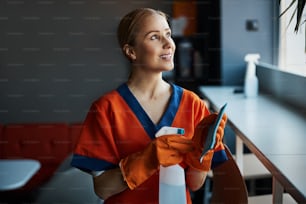 Waist-up portrait of an attractive cleaner with a plastic spray bottle and an absorbent cloth looking up