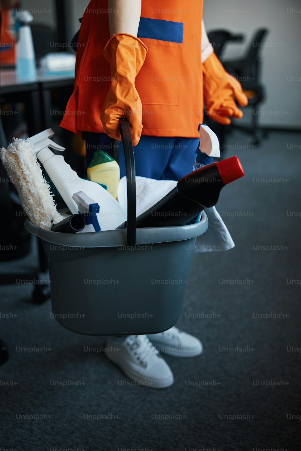 양손으로 청소 제품이 담긴 플라스틱 양동이를 들고 있는 여성 청소부의 자른 사진