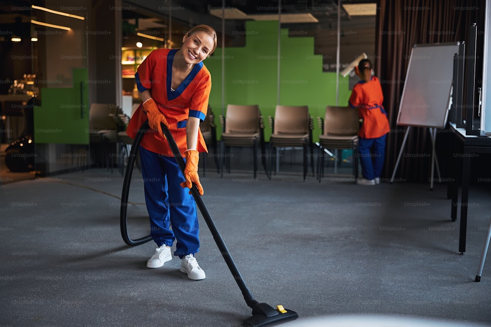 Smiling lovely female worker with a telescopic vacuum cleaner wand in her hands looking ahead