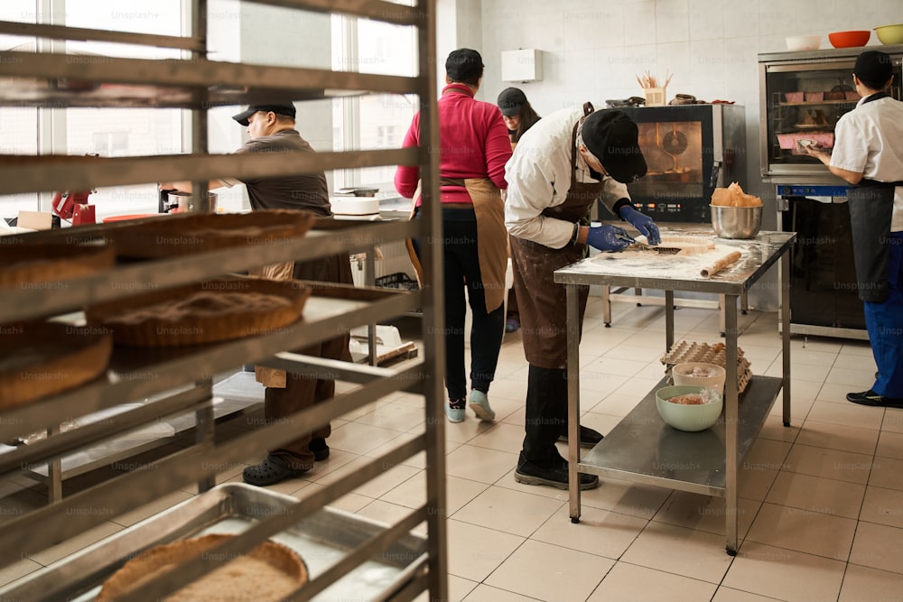 Proceso de cocción. Vista de cuerpo entero de la cocina con los trabajadores preparando una sabrosa panadería para el salling. Todo el mundo está ocupado con su propio proceso. Foto de archivo