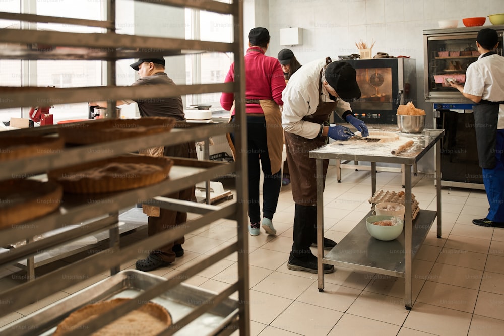 Kochprozess. Ganzkörperansicht der Küche mit Arbeitern, die leckere Bäckerei für den Verkauf vorbereiten. Jeder ist mit seinem eigenen Prozess beschäftigt. Archivfoto