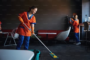 Group of young Caucasian professional janitors in uniforms doing the cleaning in the office cafeteria