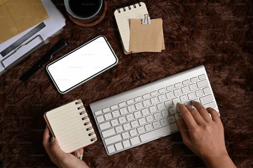 Oben Ansicht einer Frau, die auf einer drahtlosen Tastatur tippt und ein Notebook über einen braunen Pelzteppich hält.