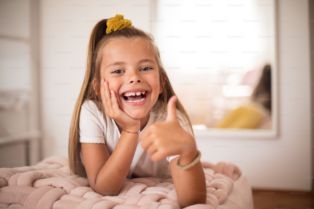 Smiling little girl with thumb up  in bedroom alone. Looking at camera.