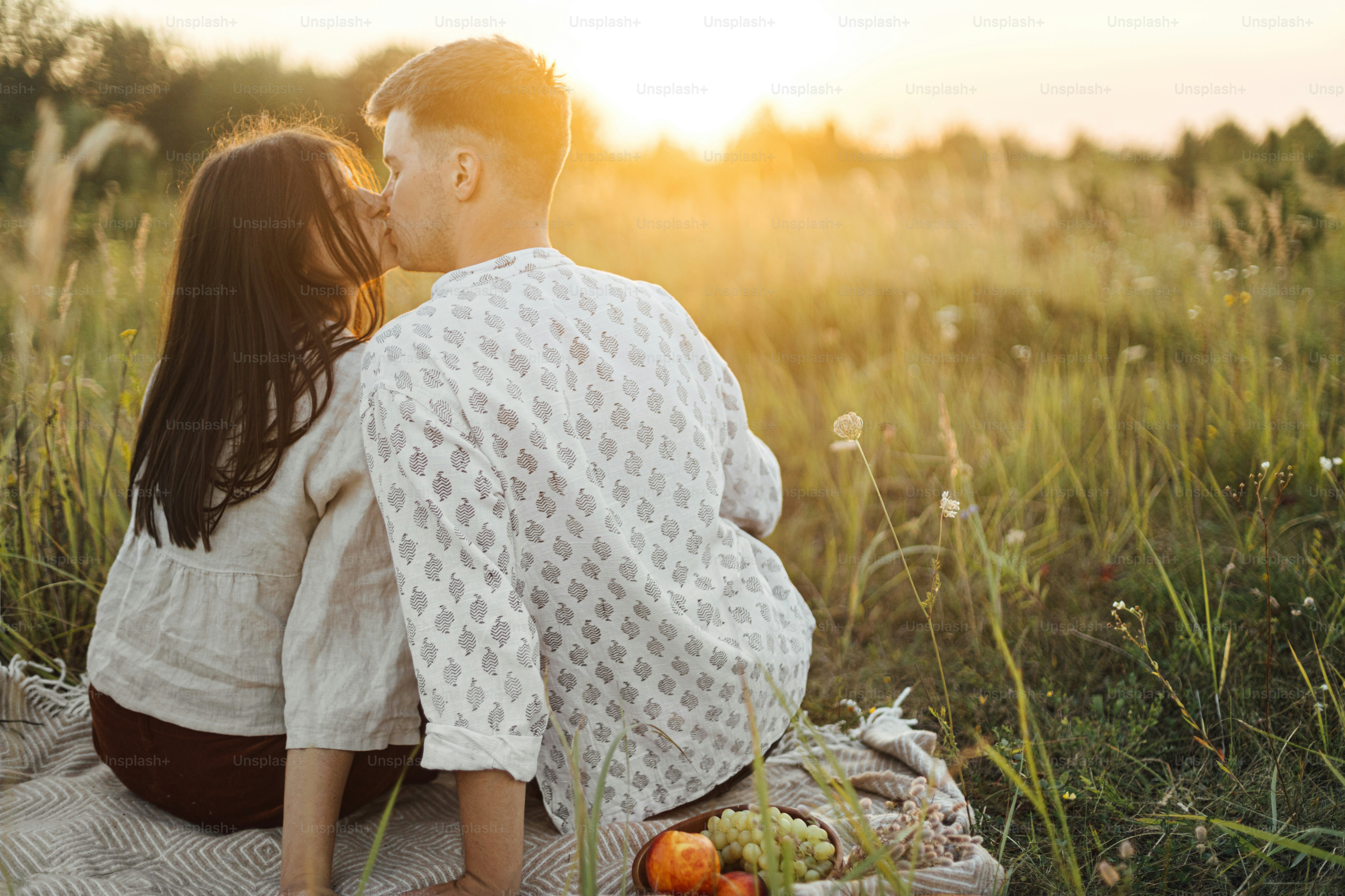 Elegante pareja hermosa besándose en manta en luz cálida y soleada entre la  hierba en el prado de verano, disfrutando de la puesta de sol. Vacaciones y  picnic. Joven familia boho abrazando,, image size:3000x2000