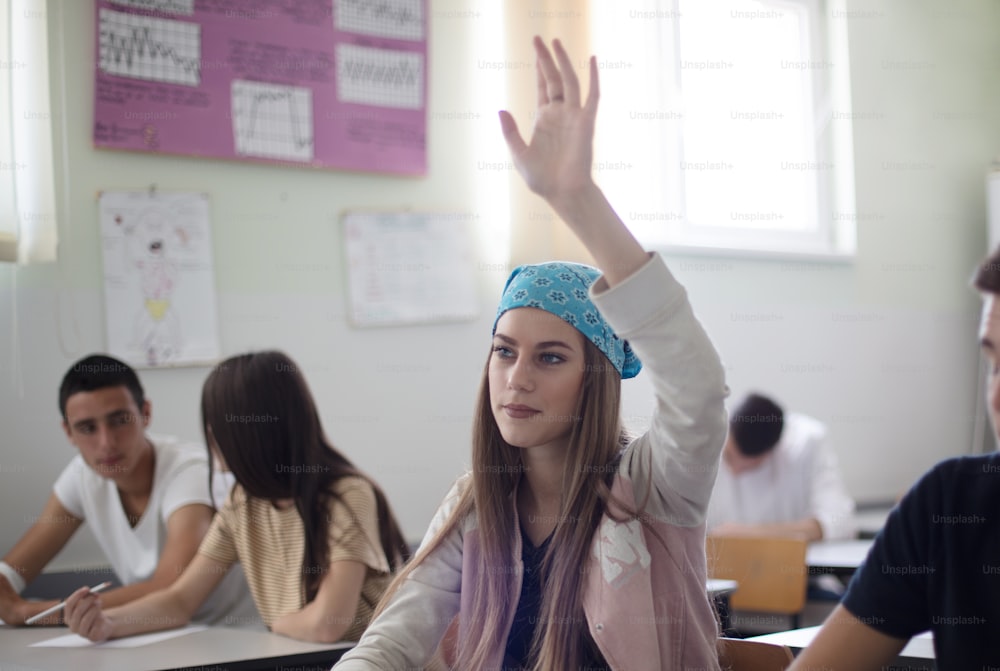 She is smart. Teenagers student girl sitting in the classroom and raising hand.