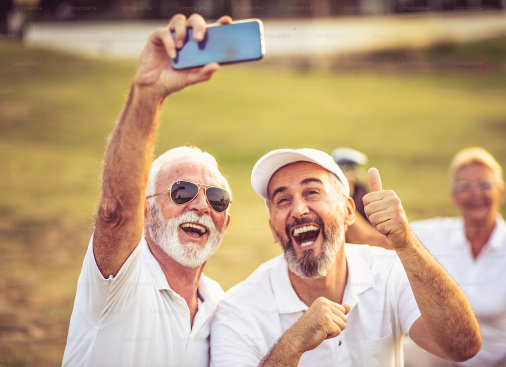 Golfeurs seniors utilisant leur téléphone et prenant un autoportrait. La mise au point se fait sur le premier plan.