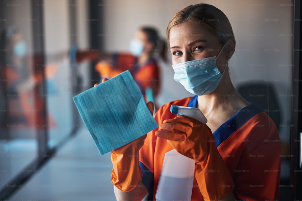 Portrait of a female worker in a face mask and rubber gloves posing for the camera during the office cleaning