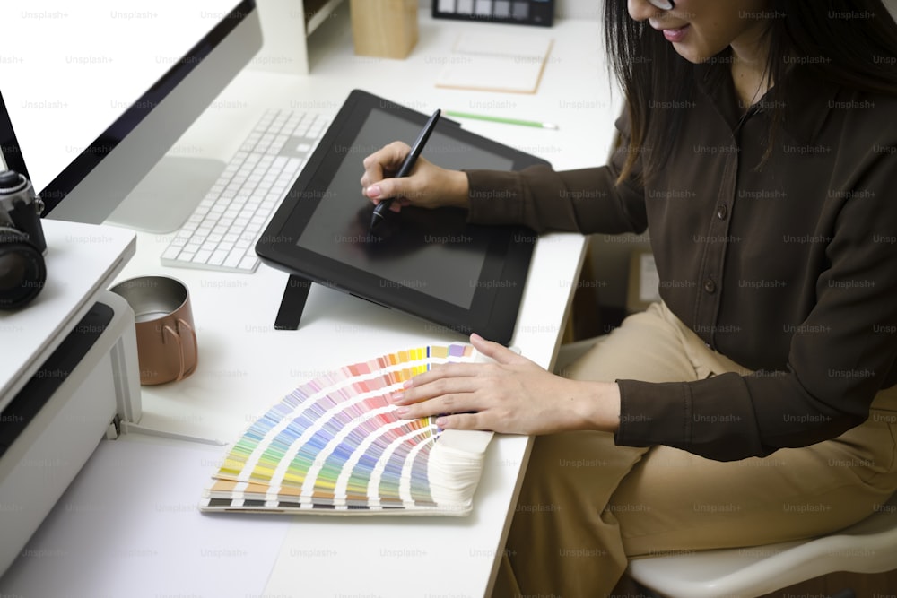 Plan recadré d’un graphiste souriant travaillant avec une tablette graphique et un échantillon de couleur sur un lieu de travail moderne.