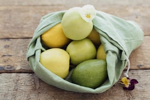 Eco friendly plastic free grocery delivery and shopping. Fresh apples, avocado, lemons in cotton bag with flower on rustic wooden table. Zero waste. Organic fruits and vegetables in reusable bag