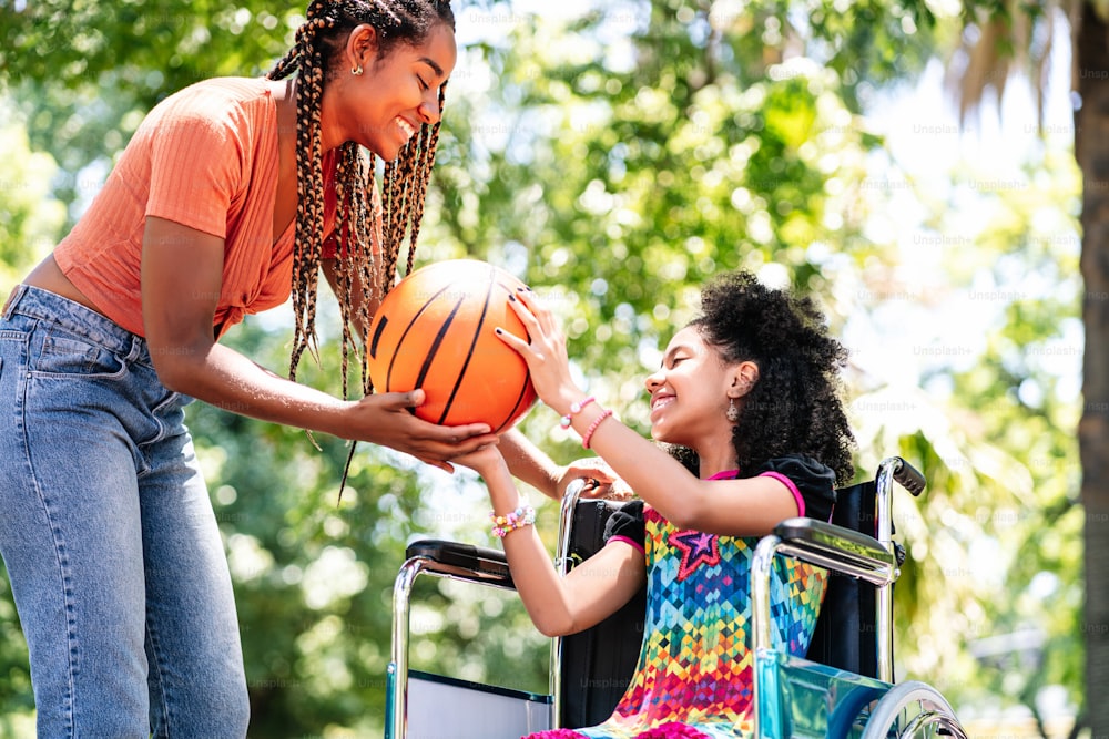 A little girl in a wheelchair having fun with her mother while playing basketball together at park.