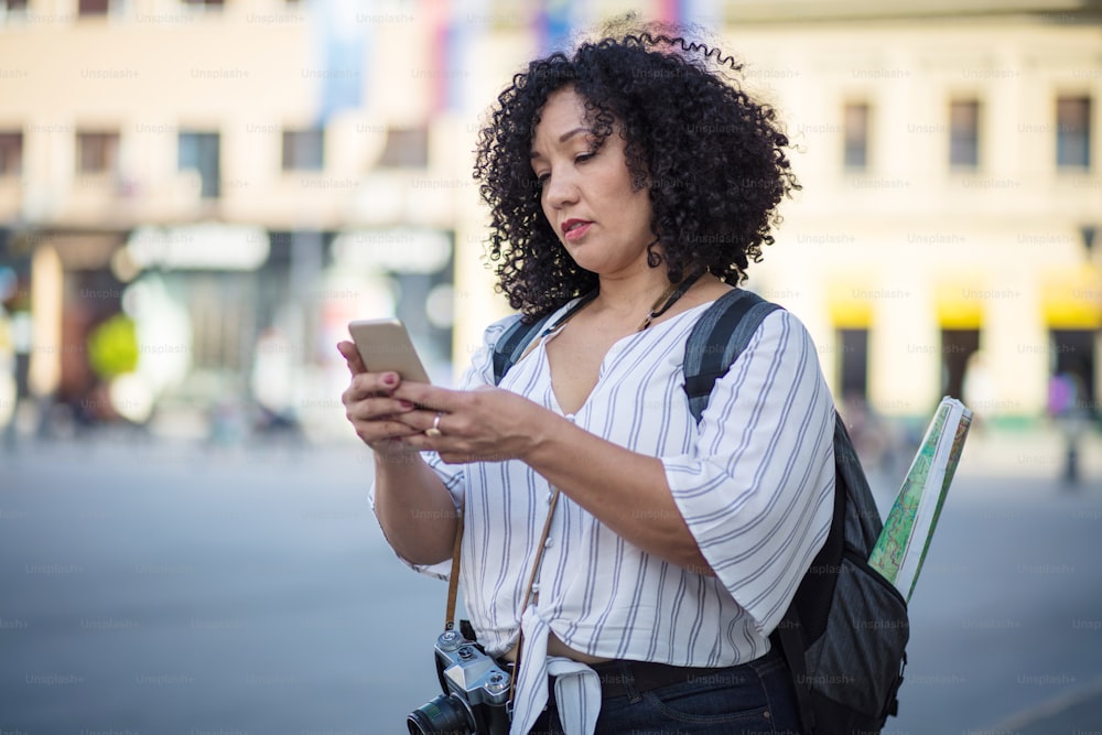 Mulher turista em pé na rua e usando o telefone inteligente.