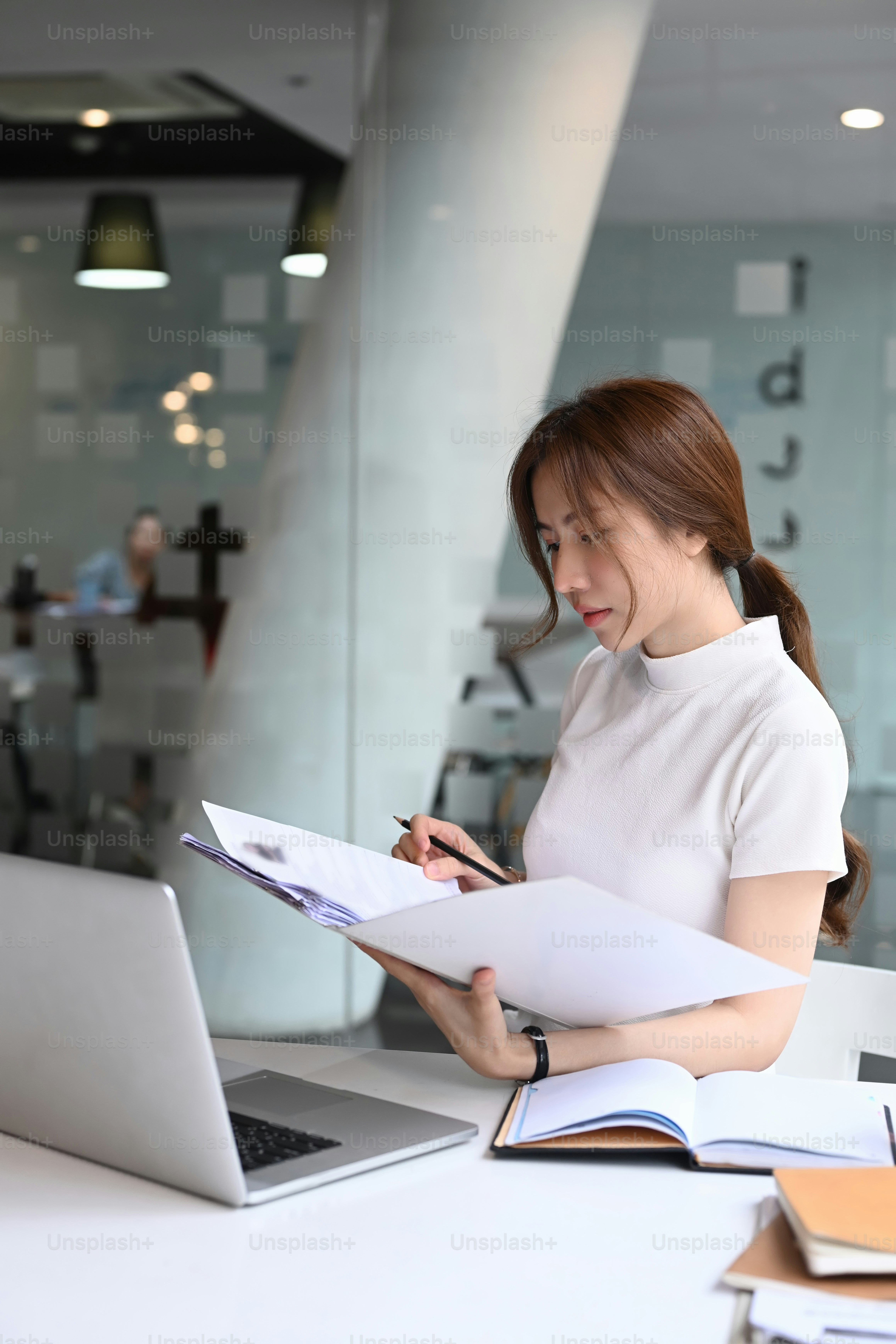 Asian businesswoman sitting in front of computer laptop and analyzing financial data on document in modern office