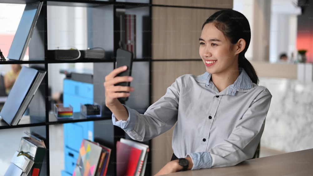 Smiling asian businesswoman making video call via smartphone while sitting in office.
