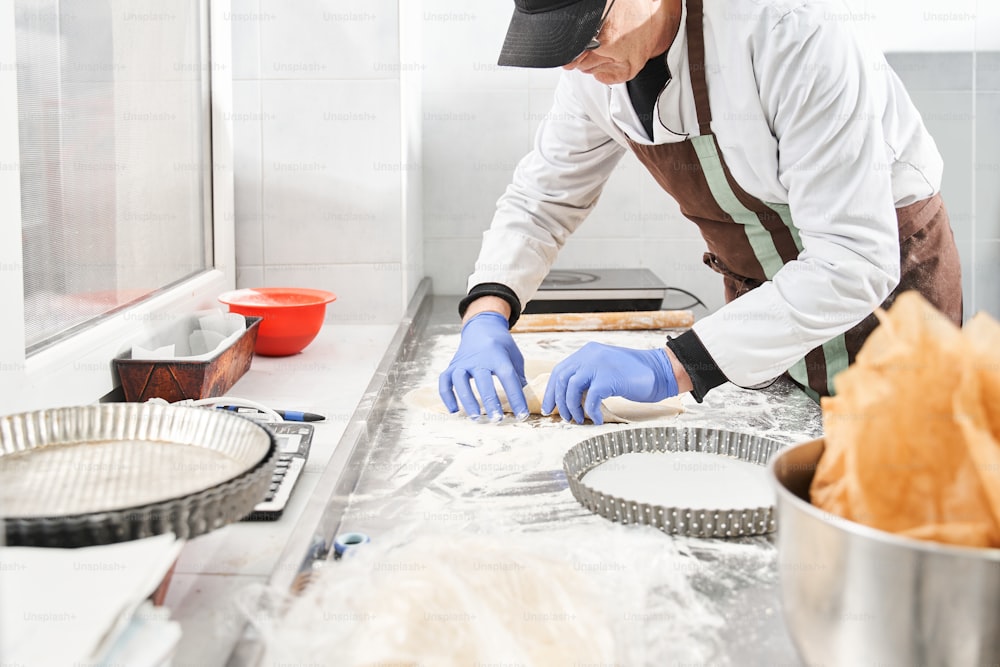 Horizontal view of the baker man kneading dough on table with flour while making pie. Cooking at baker house at the kitchen concept. Stock photo